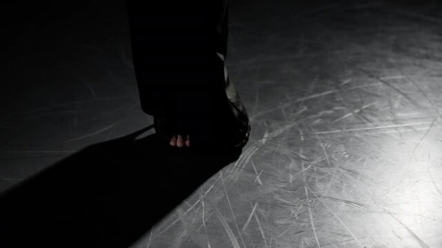 Dancer wearing high heels is gracefully moving her feet on a dance floor, illuminated by dramatic lighting that casts long shadows