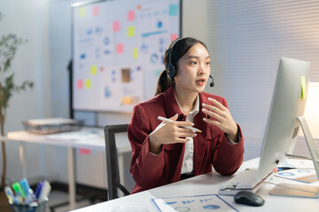 Businesswoman is speaking on a video call while working late in an office building. She is gesturing with her hands and using a headset