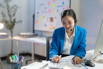 Focused asian businesswoman in modern office analyzing charts on laptop with headset, showcasing professionalism and expertise in marketing and research