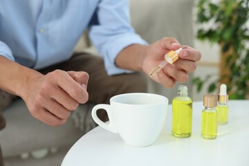 Young man dripping CBD tincture into drink at white table, closeup