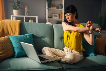 Asian woman stretching arm while working on a laptop at home couch