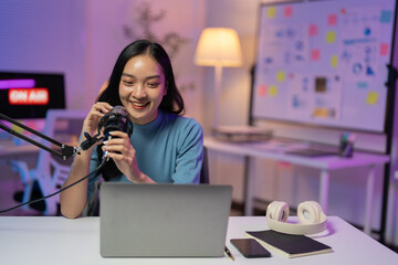 Asian woman records a podcast in her cozy home studio, surrounded by modern equipment and neon lights, embracing the world of digital media and entertainment - Powered by Adobe