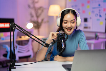 Content creator recording audio blog using a professional microphone and headphones, she is smiling and looking at a laptop