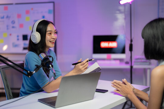Two women are recording an audio podcast in a home recording studio, one speaking into a professional microphone and the other listening