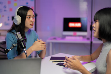 Two young women passionately recording a podcast in a cozy home studio. Engaging in lively conversation on a relevant topic