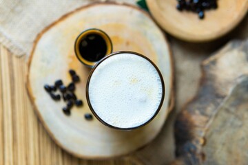 Glass of cappuccino with foam and espresso in natural background and wood elements