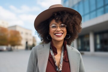 Portrait of a merry afro-american woman in her 40s donning a classic fedora while standing against modern university campus background