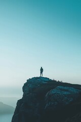 A solitary person stands on a rocky mountain peak, silhouetted against an expansive, tranquil sky conveying solitude.