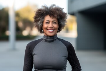Portrait of a blissful afro-american woman in her 50s showing off a lightweight base layer while standing against modern university campus background