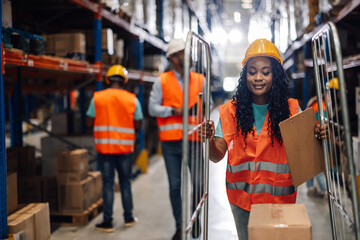 Smiling warehouse worker pushing trolley checking inventory