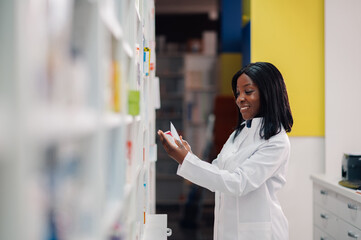 Smiling diverse female druggist holding creme tubes at pharmacy shop.