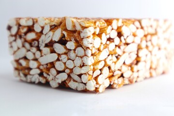 A close-up of a rectangular block of puffed rice treats. The treats are a golden brown color and are coated in a sticky, sweet substance. The block is sitting on a white background.