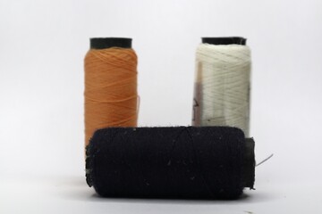 A close-up of three spools of thread against a white background. The spools are arranged in a row and are of different colors: orange, navy blue, and white.