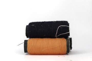 A close-up of three spools of thread against a white background. The spools are arranged in a row and are of different colors: orange, navy blue, and white.