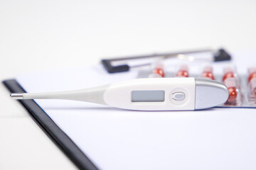 Fototapeta premium Electronic thermometer and pills on white background. Medical equipment.