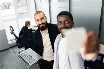 Multiracial colleagues collaborate in modern office environment. one holds laptop, other engages with notes, showcasing teamwork, technology, and professional camaraderie.