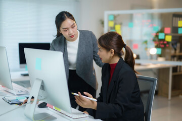 Two asian businesswomen are having a discussion while looking at a desktop computer in a modern office