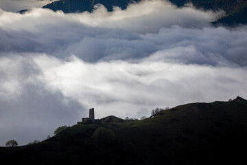 Medieval tower on mount  above clouds, with snowy peaks in the background