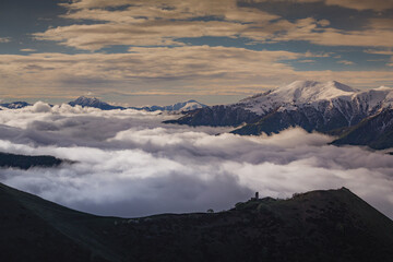 Medieval tower on mount  above clouds, with snowy peaks in the background