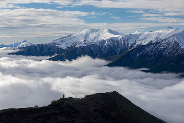 Medieval tower on mount  above clouds, with snowy peaks in the background