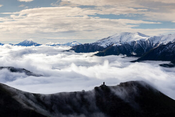 medieval tower on mountain above clouds, with snowy mountain picks, cloud flows over mountain ridge