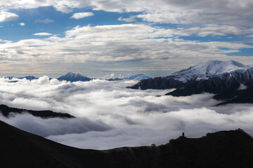 Medieval tower on mount  above clouds, with snowy peaks in the background