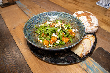 A plate of delicious Maple-Roasted squash and feta cheese with bread rolls placed on a wooden kitchen table