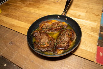 A pan of three delicious stakes being cooked in butter in a large pan on a wooden kitchen table work top