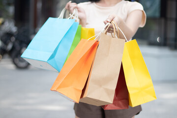 Young middle-aged Asian woman using a cell phone and carrying shopping bags outside her home on a city street.