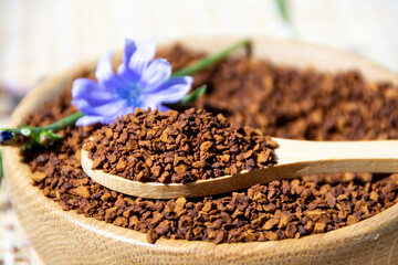 Ground chicory root on a wooden spoon and chicory flowers on a rustic wooden background. Alternative medicine. Healthy drinks. chicory drink