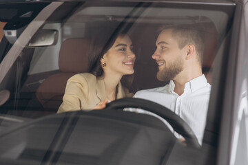 Portrait of smiling beautiful couple sitting in modern luxury car, happy excited young man and woman buying new car in dealership.