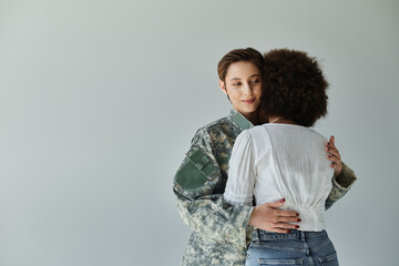 A heartfelt embrace as a military soldier bids farewell to her wife in a cozy studio setting.