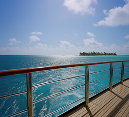 ocean, captured from the deck of a luxurious yacht.  polished wooden railing with crystal-clear turquoise water stretching out before it. In the distance, a tropical island with lush, green palm trees