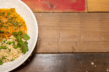 A plate of delicious chicken tikka masala and rice with peas on a wooden kitchen work top background