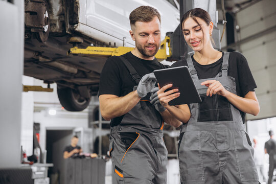 Young expert female inspects repair checklist with automotive mechanic worker partner, quality suspension technician team at fix garage. Vehicle maintenance service works industry occupation job. - Powered by Adobe