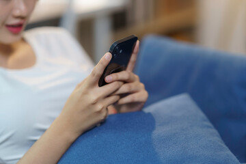 Young woman is lying on a blue couch using a smartphone, browsing social media