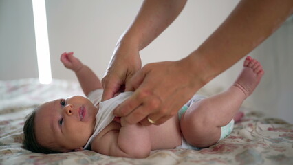 Parent gently dresses baby on bed while baby looks up, arms raised, intimate home environment with natural emotions, focusing on care, comfort, and bonding moments