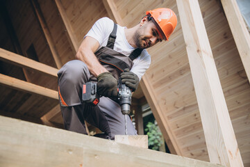 Construction worker working with screwdriver on wooden frame, diy eco-friendly homes concept. Man...