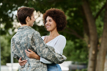 Fototapeta premium A young female soldier in camouflage is joyfully welcomed by her loving wife upon returning home.