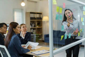 Business team having a meeting in a modern office with a businesswoman leading the discussion using sticky notes on a glass wall