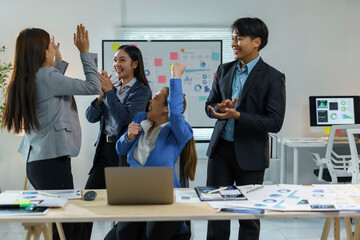 Team of businesspeople is celebrating their success by giving high fives in a modern office