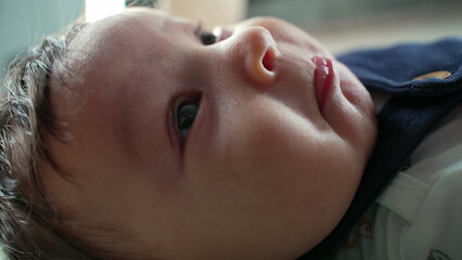 Close-up of a baby lying on their back with an inquisitive expression, gazing upwards with wide eyes. natural lighting highlights the soft textures of the baby’s face and skin