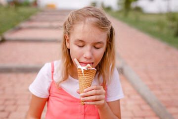 A girl in a pink tunic is sitting on a summer lawn and eating delicious ice cream