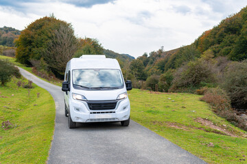 front photo of a white camper van in motion driving on a mountain and forest road in nature at...