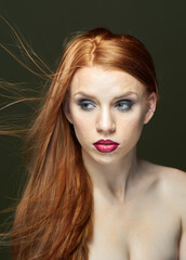 Woman with red hair and red lipstick poses for a photo. She has thick, beautiful hair. Fashion and beauty concept.