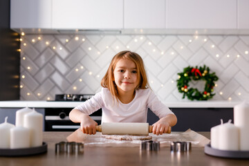 The girl is preparing gingerbread dough in the kitchen, radiating Christmas cheer