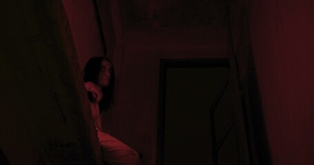 Horror scene of a mysterious Scary Asian ghost woman creepy have hair covering the face sitting on staircase at abandoned house with background dark scene movie at night, festival Halloween concept