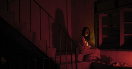 Horror scene of a mysterious Scary Asian ghost woman creepy have hair covering the face sitting on staircase at abandoned house with background dark scene movie at night, festival Halloween concept