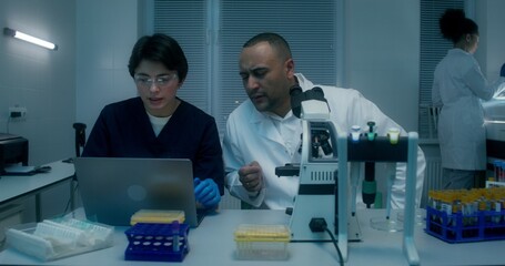 Work in a medical laboratory. A man and a woman are talking using a laptop sitting at a table with a microscope. A woman sets up a blood splitting device