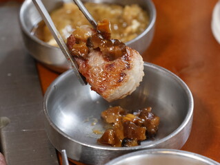 a piece of Korean Pork belly(samgyeopsal) meat meat with chopsticks in front of a bowl of sauce
